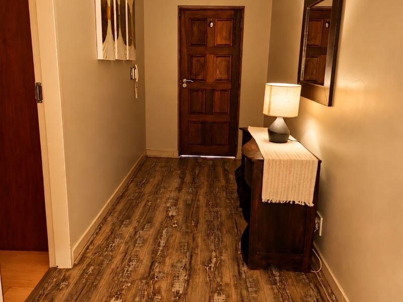 A well-maintained hallway featuring wood-look laminate flooring, neutral wall tones, and a solid timber entrance door.
