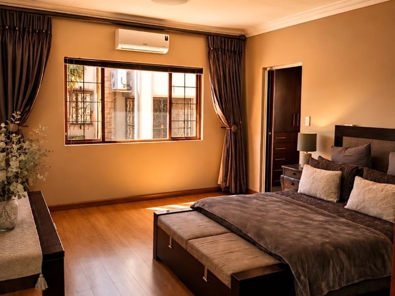 A well-maintained bedroom featuring warm laminate flooring, a split-system air conditioner, and built-in storage, offering a comfortable and inviting living space.