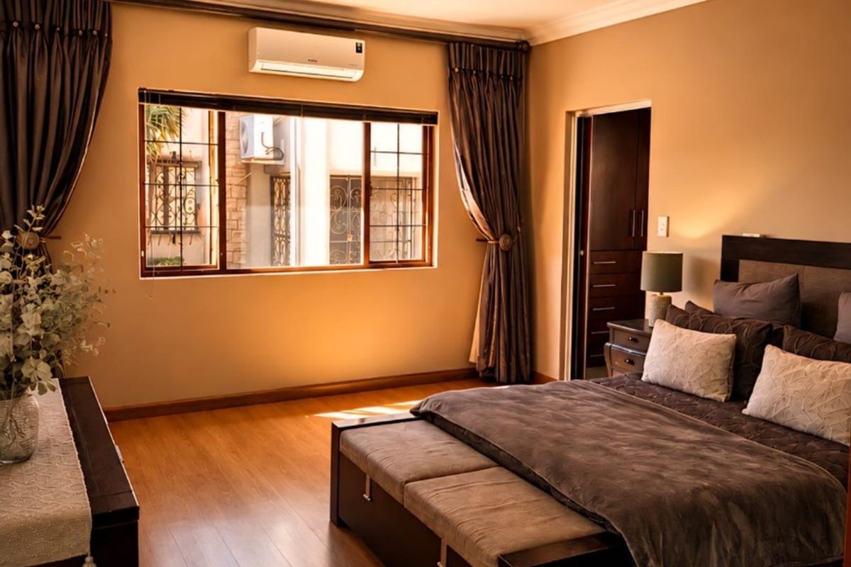 A well-maintained bedroom featuring warm laminate flooring, a split-system air conditioner, and built-in storage, offering a comfortable and inviting living space.