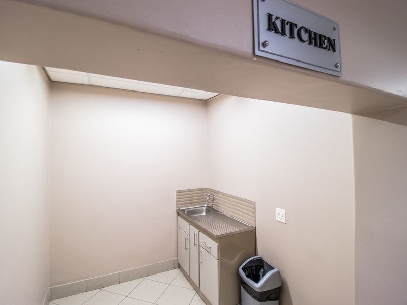 A compact commercial kitchen area featuring a stainless steel sink, tiled backsplash, and built-in cabinetry, suitable for basic food preparation or utility use.