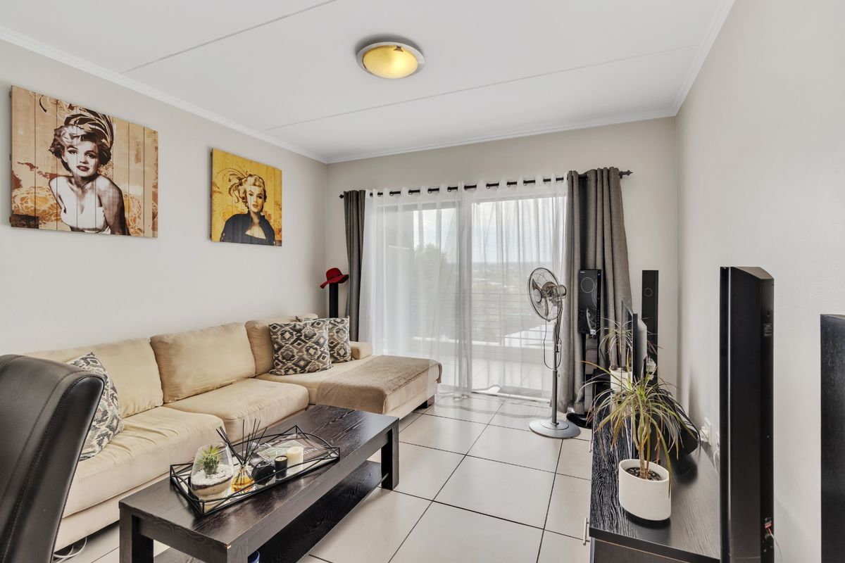 A well-lit living room featuring tiled flooring and a large sliding glass door providing access to an outdoor balcony area.