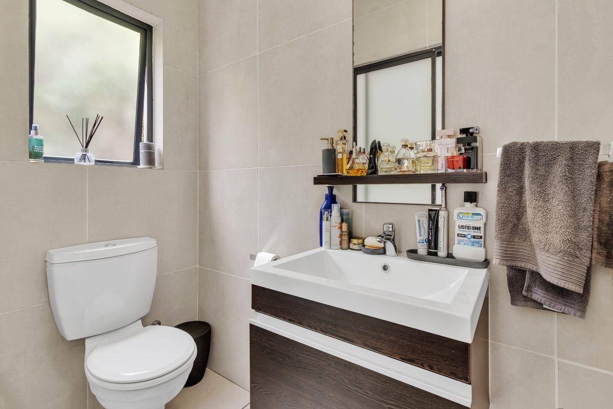 A modern bathroom featuring a dark wood vanity with a white basin, wall-mounted mirror, and neutral wall tiling.