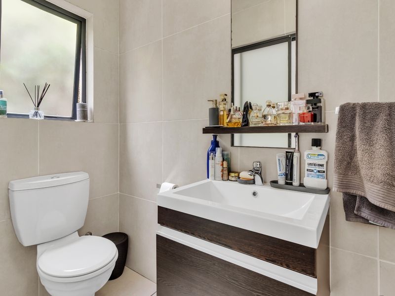 A modern bathroom featuring a dark wood vanity with a white basin, wall-mounted mirror, and neutral wall tiling.