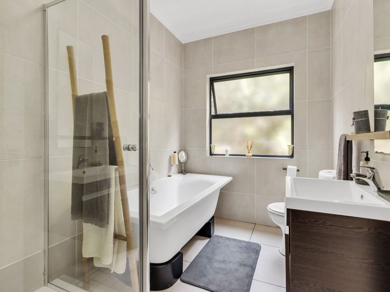 Modern bathroom featuring a freestanding bathtub, glass-enclosed shower, vanity with basin, and neutral floor-to-ceiling tiling.