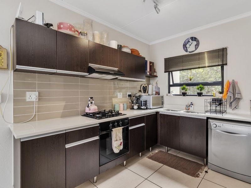 A functional kitchen featuring dark wood cabinetry, stone countertops, a gas hob with extractor fan, and tiled flooring with a neutral backsplash.
