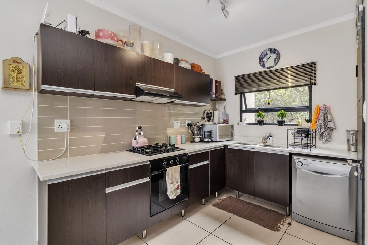 A functional kitchen featuring dark wood cabinetry, stone countertops, a gas hob with extractor fan, and tiled flooring with a neutral backsplash.