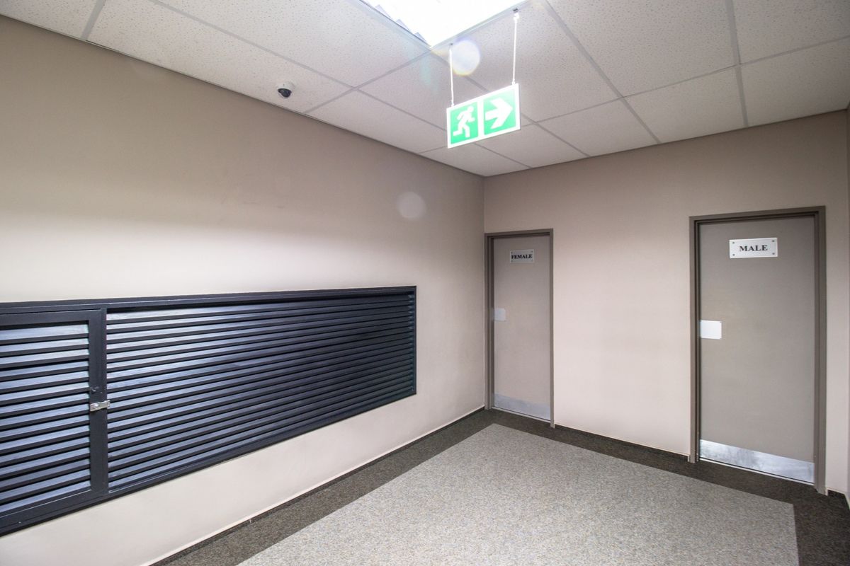 A clean commercial hallway featuring a suspended ceiling, security camera, exit signage, and separate access doors for male and female facilities.