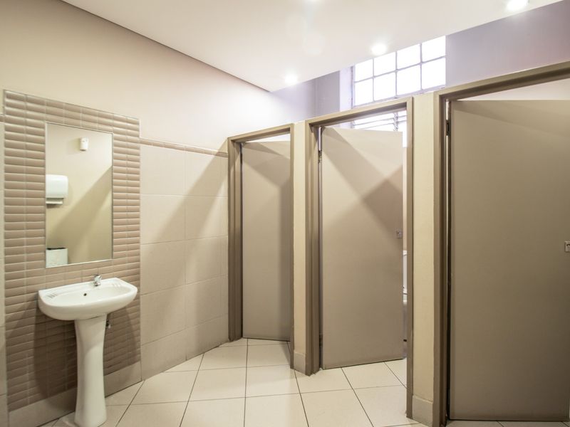 A clean and well-maintained commercial restroom featuring a pedestal washbasin, tiled walls and floors, and multiple private cubicles.