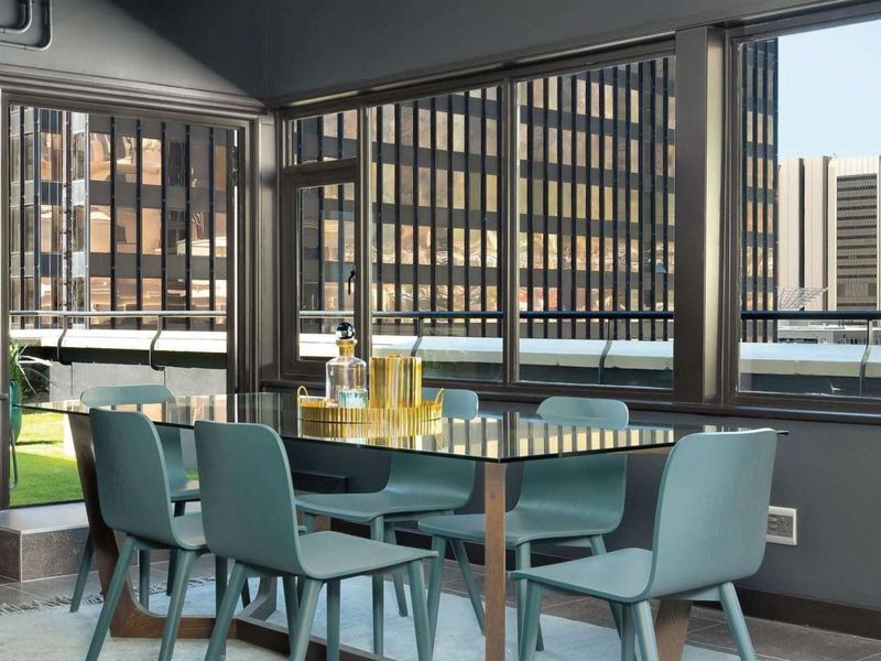 A modern dining area featuring large windows with urban views, tiled flooring, and direct access to an outdoor balcony space.