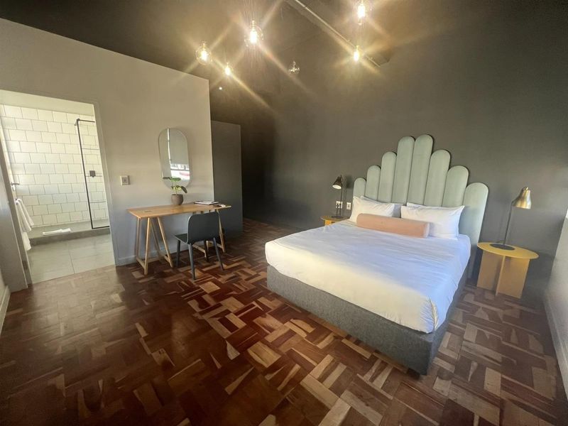 Spacious bedroom featuring warm parquet flooring, dark accent walls, and an integrated en-suite bathroom with a modern walk-in shower.