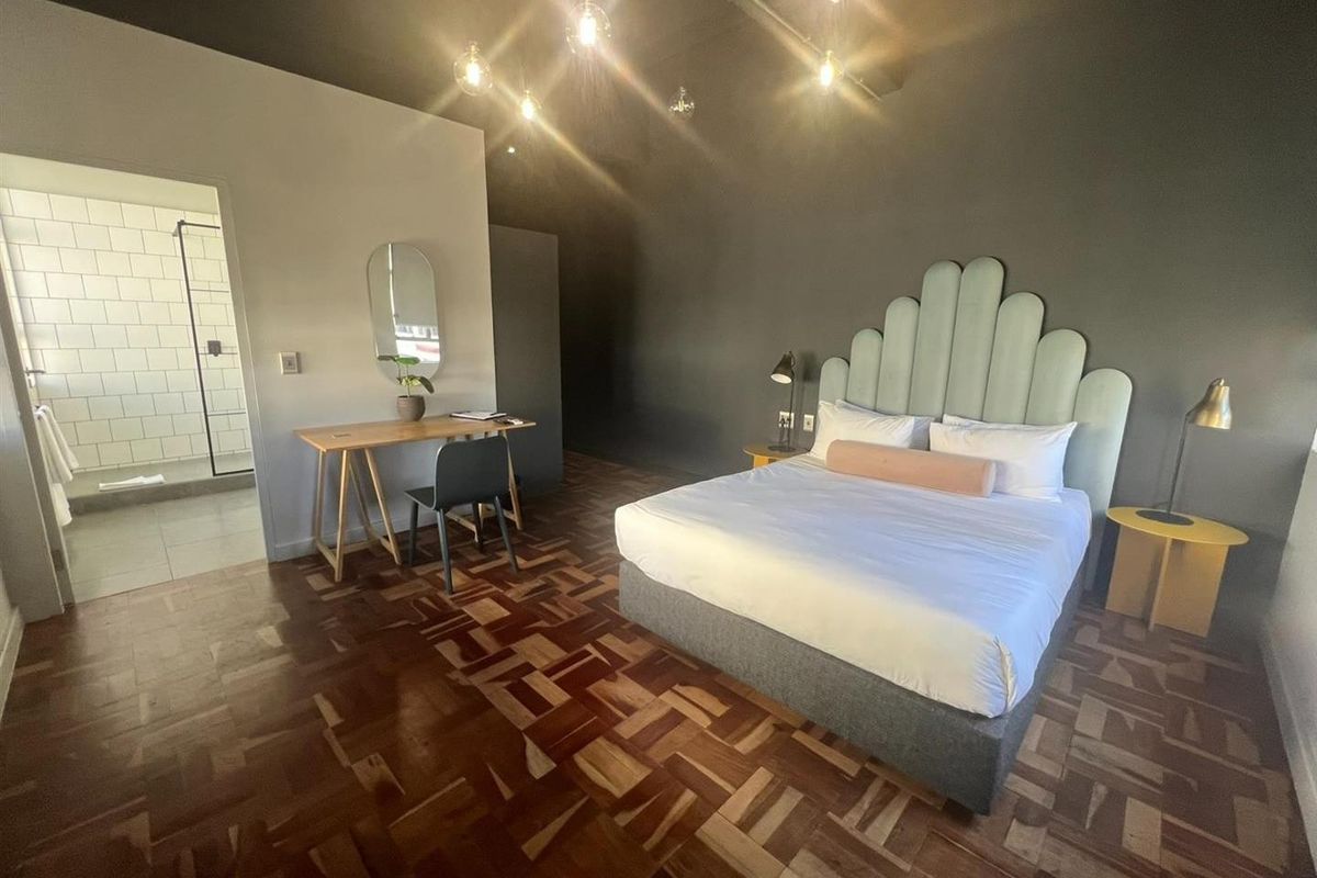 Spacious bedroom featuring warm parquet flooring, dark accent walls, and an integrated en-suite bathroom with a modern walk-in shower.