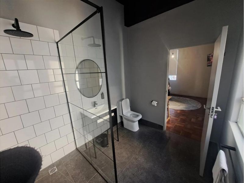 Modern bathroom featuring a walk-in shower with a black-framed glass screen, subway-tiled shower wall, vanity basin, and toilet.