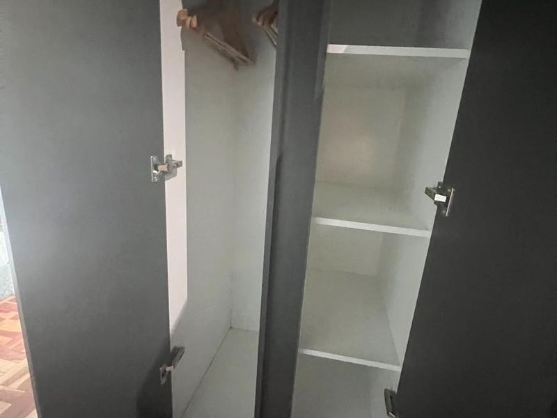 A built-in bedroom wardrobe featuring dark exterior doors, internal shelving, and a hanging rail for storage.