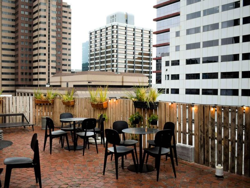 An urban rooftop patio featuring brick paving and timber slat fencing, offering an elevated outdoor space with city skyline views.