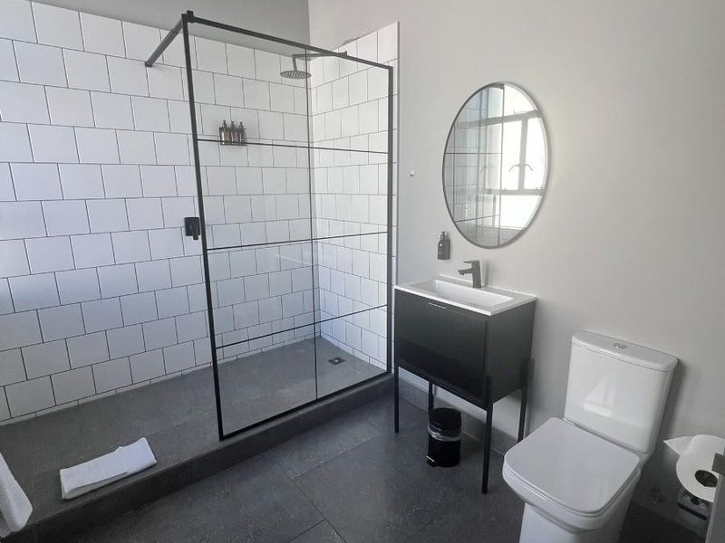 Modern bathroom featuring a walk-in shower with black-framed glass screen, subway tiling, vanity unit with basin, and a contemporary toilet.