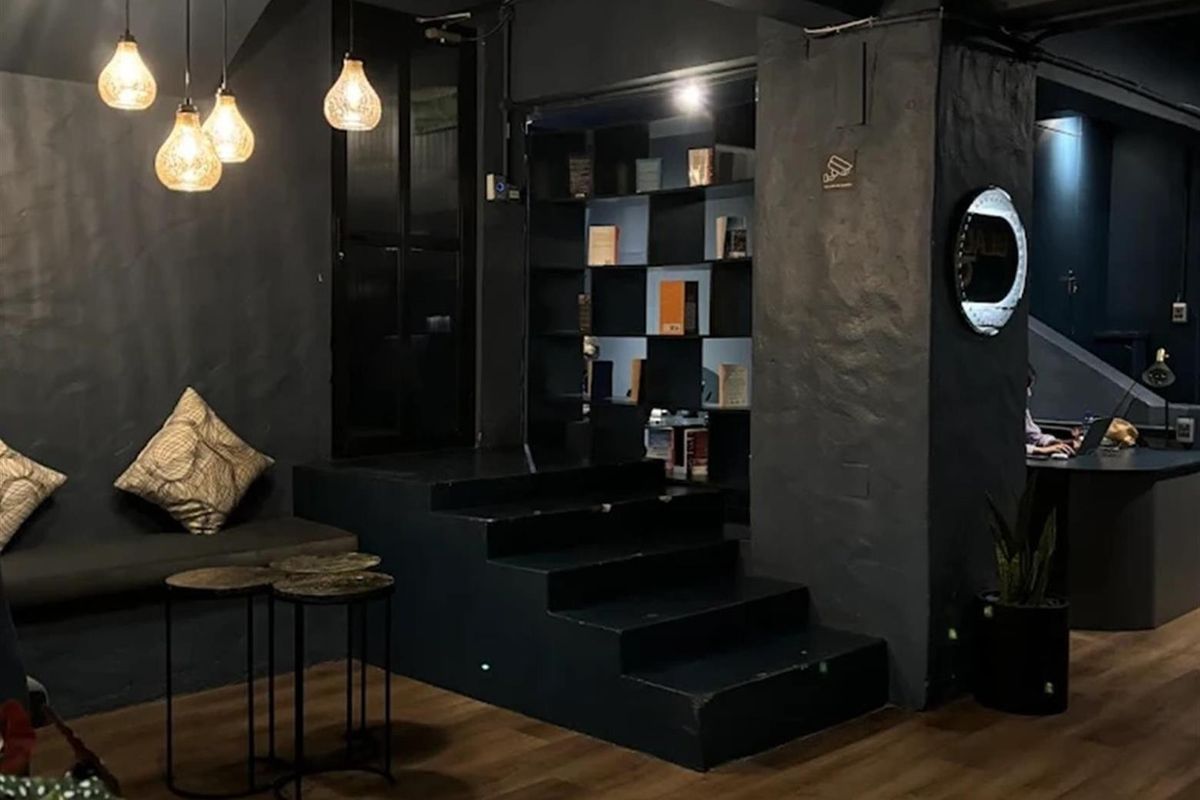 A modern, dark-themed living area featuring a raised platform, built-in shelving, and stylish pendant lighting, creating a sophisticated and moody atmosphere.