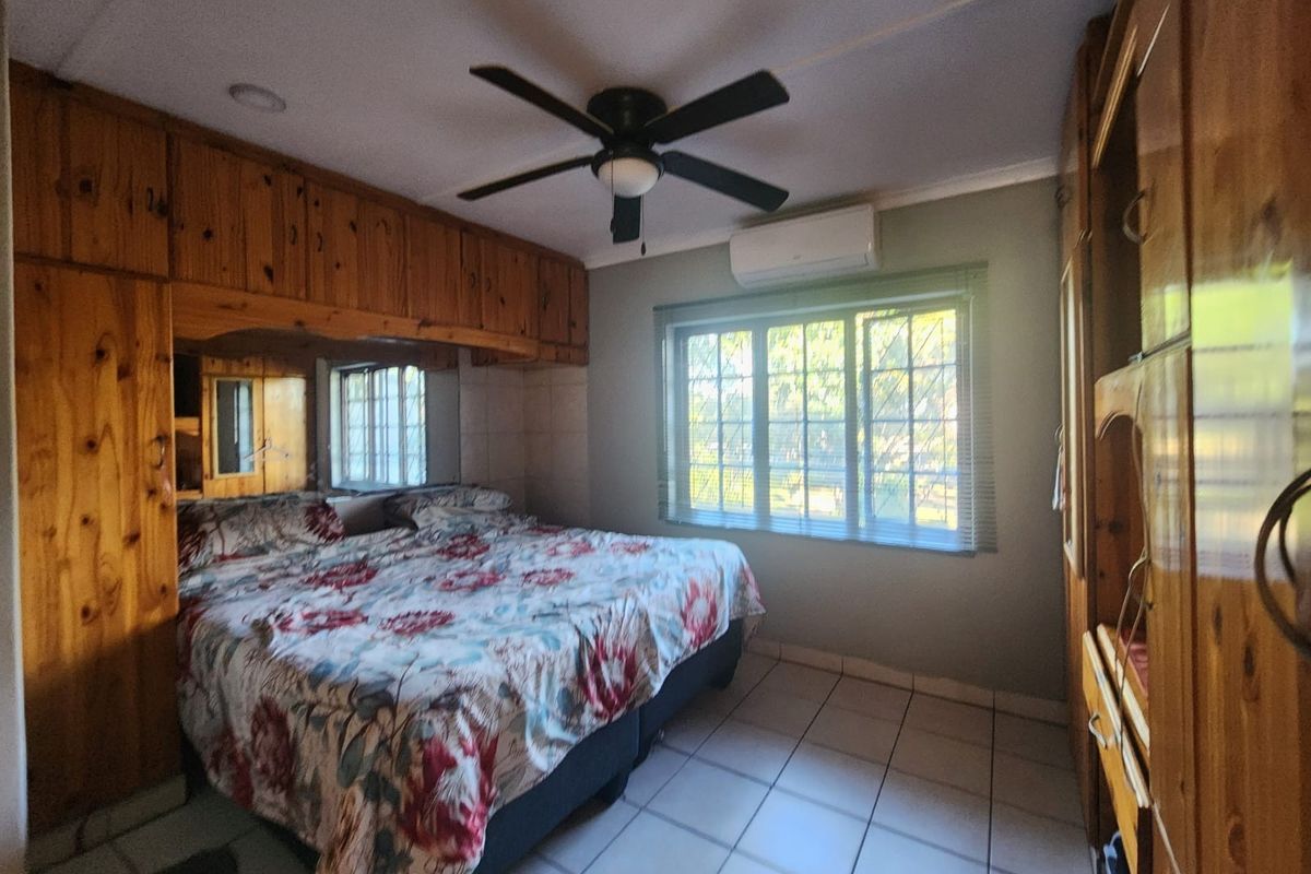 A bedroom featuring tiled flooring, built-in wooden cabinetry, a ceiling fan, and a wall-mounted air conditioning unit.