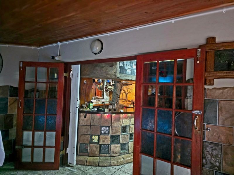 A rustic-style indoor bar area featuring a stone-clad counter, timber ceiling, and double french doors leading into the space.