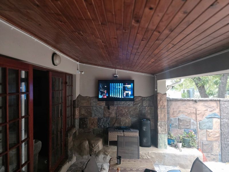 Covered patio area featuring a timber-clad ceiling, stone-cladding feature wall, and tiled flooring, providing a functional outdoor entertainment space.
