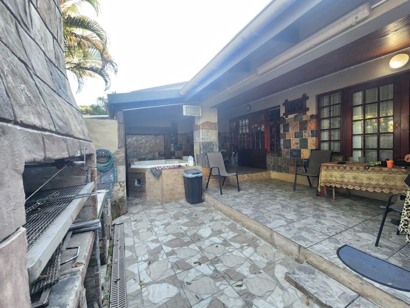 Covered patio area featuring a built-in braai, stone-clad walls, and a built-in jacuzzi, providing a functional outdoor entertainment space.