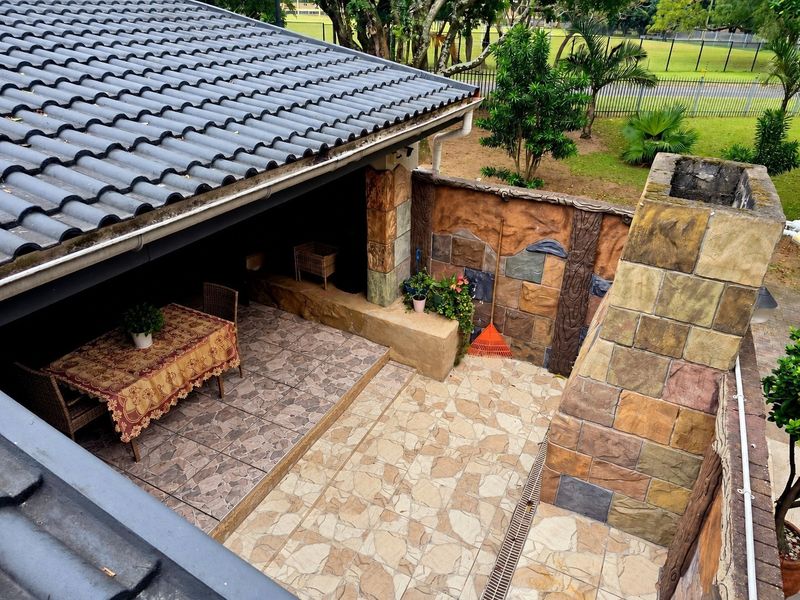 Covered outdoor patio featuring a built-in stone fireplace, tiled flooring, and decorative stone wall cladding, overlooking a garden area.