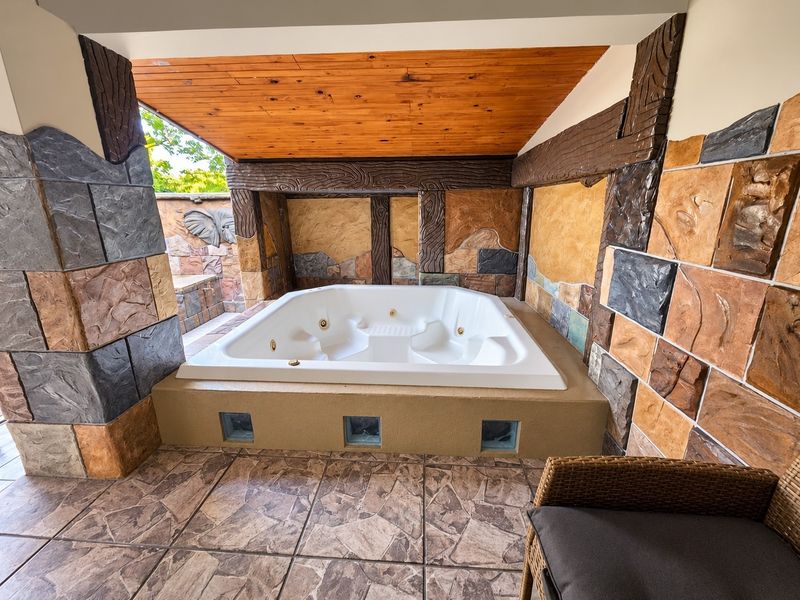 A covered outdoor patio area featuring a built-in jacuzzi, decorative stone wall cladding, and a warm timber ceiling finish.