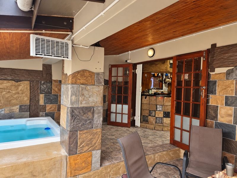 Covered patio area featuring a built-in jacuzzi, stone-clad walls, timber ceiling, and direct access to an indoor bar area through wooden french doors.