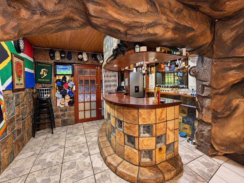 A unique, custom-built indoor bar area featuring a faux rock structure, stone-tiled bar counter with glass block accents, and timber ceiling finishes.