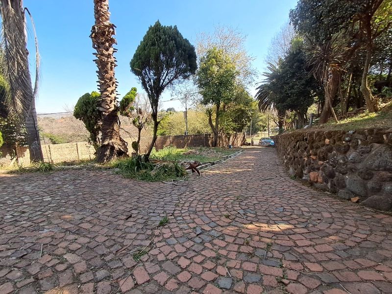 A spacious rear garden area featuring a cobblestone driveway, stone retaining walls, and established mature trees.