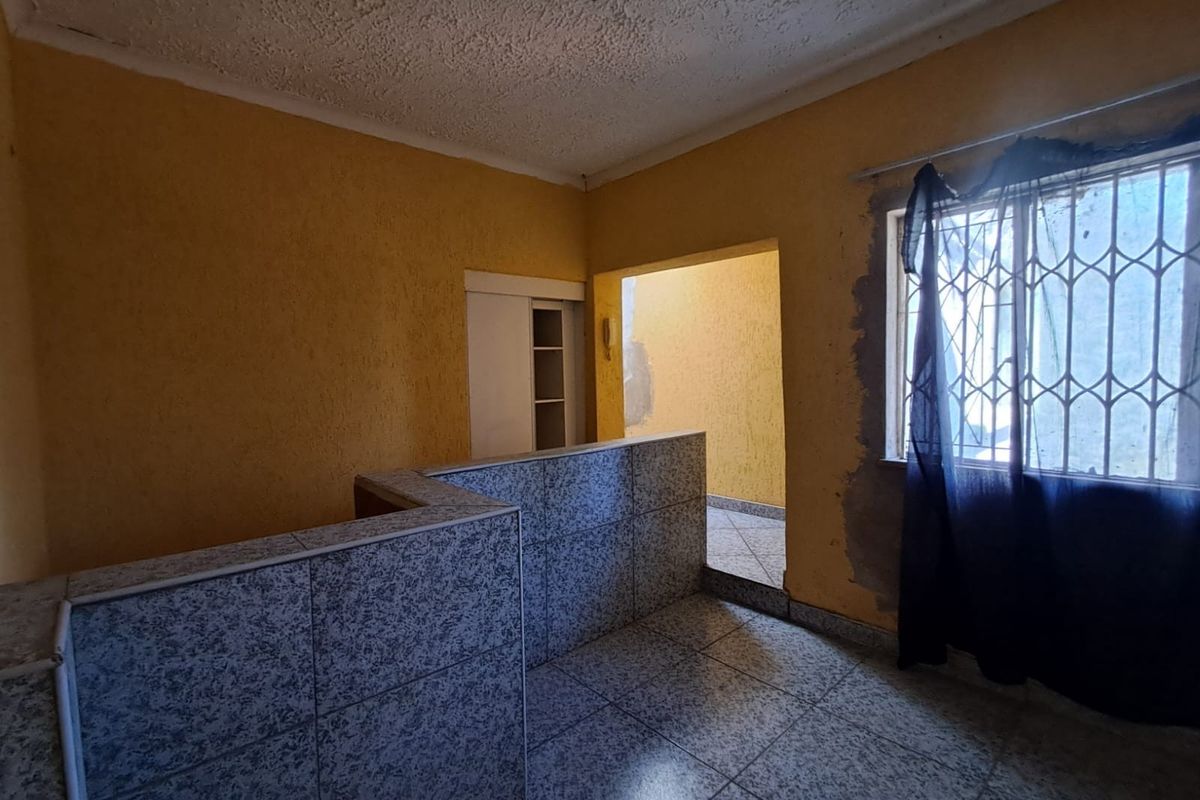 An empty living area featuring tiled flooring, a tiled partition wall, and a built-in cupboard, requiring cosmetic updates and wall repairs.
