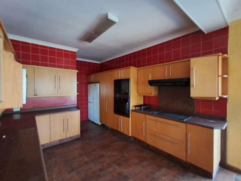 A spacious kitchen featuring built-in cabinetry, integrated oven and hob, and red tiled splashbacks, offering a functional layout ready for modernization.