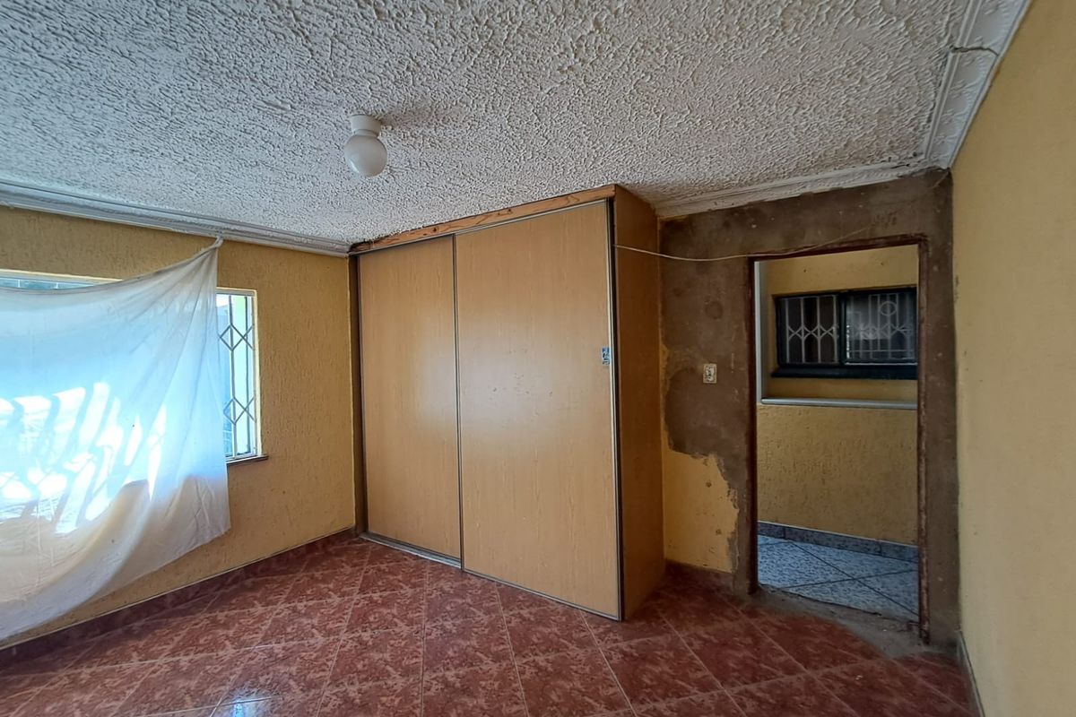 A bedroom featuring built-in wardrobes, tiled flooring, and security bars on windows, requiring cosmetic repairs to wall plaster and finishes.