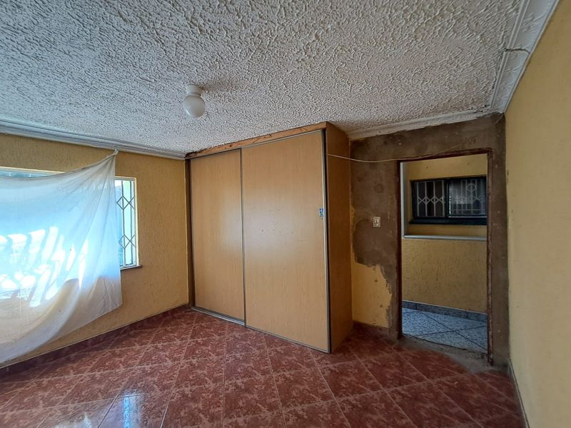 A bedroom featuring built-in wardrobes, tiled flooring, and security bars on windows, requiring cosmetic repairs to wall plaster and finishes.