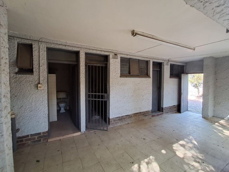 A covered utility area featuring tiled flooring, a security gate, and an external toilet, showing signs of age and requiring maintenance.