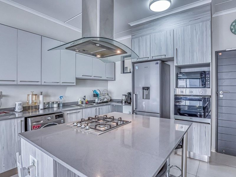 Modern kitchen featuring a central island with a gas hob, stone countertops, integrated appliances, and contemporary grey cabinetry.