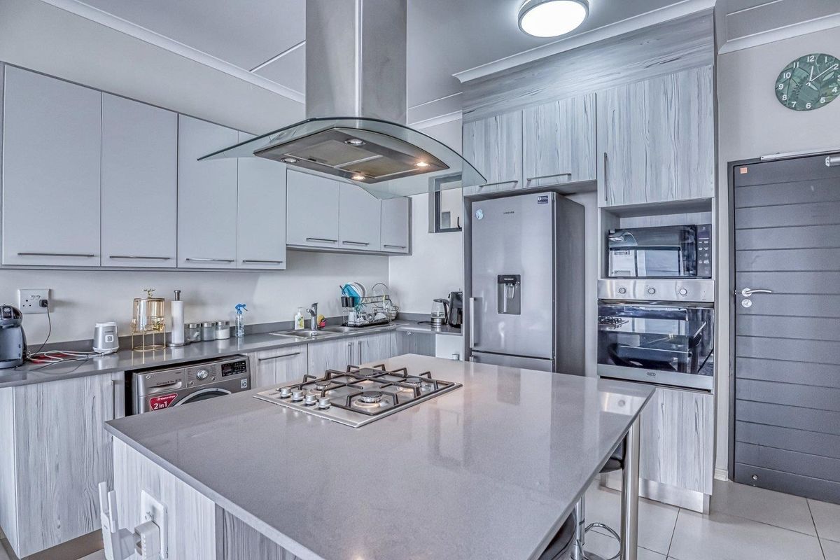 Modern kitchen featuring a central island with a gas hob, stone countertops, integrated appliances, and contemporary grey cabinetry.