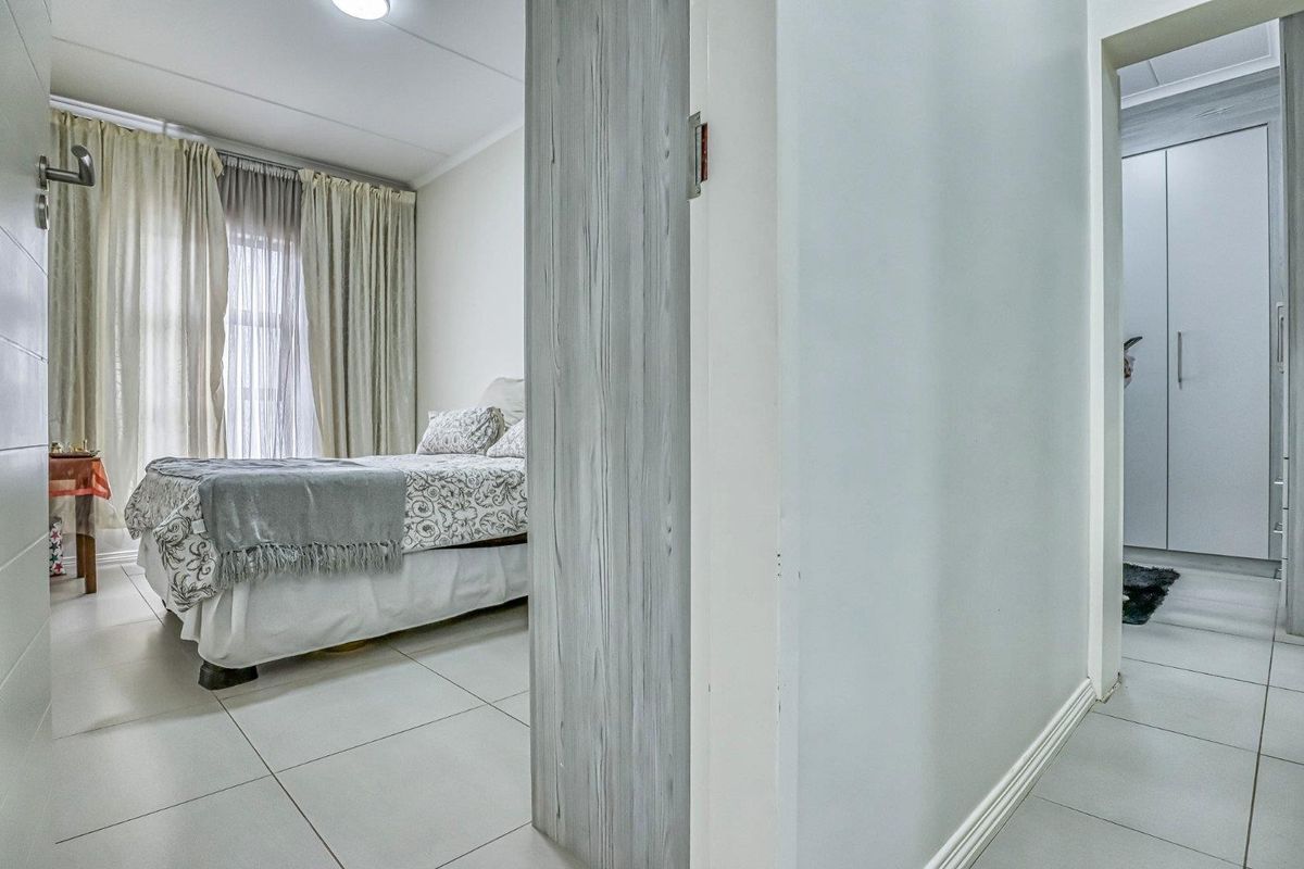 A well-maintained bedroom featuring tiled flooring and built-in cupboards, with a view into the adjacent hallway and storage area.