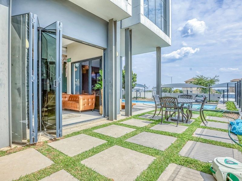 Modern patio area featuring bi-fold glass doors connecting to the living space, overlooking a private swimming pool and landscaped paved garden.