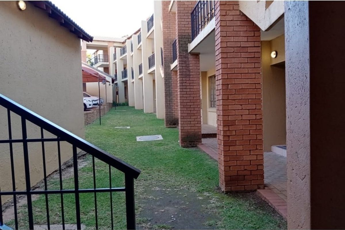 Exterior view of the apartment complex featuring brick pillars, metal railings, and a shared lawn area with paved walkways.