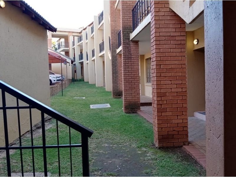 Exterior view of the apartment complex featuring brick pillars, metal railings, and a shared lawn area with paved walkways.