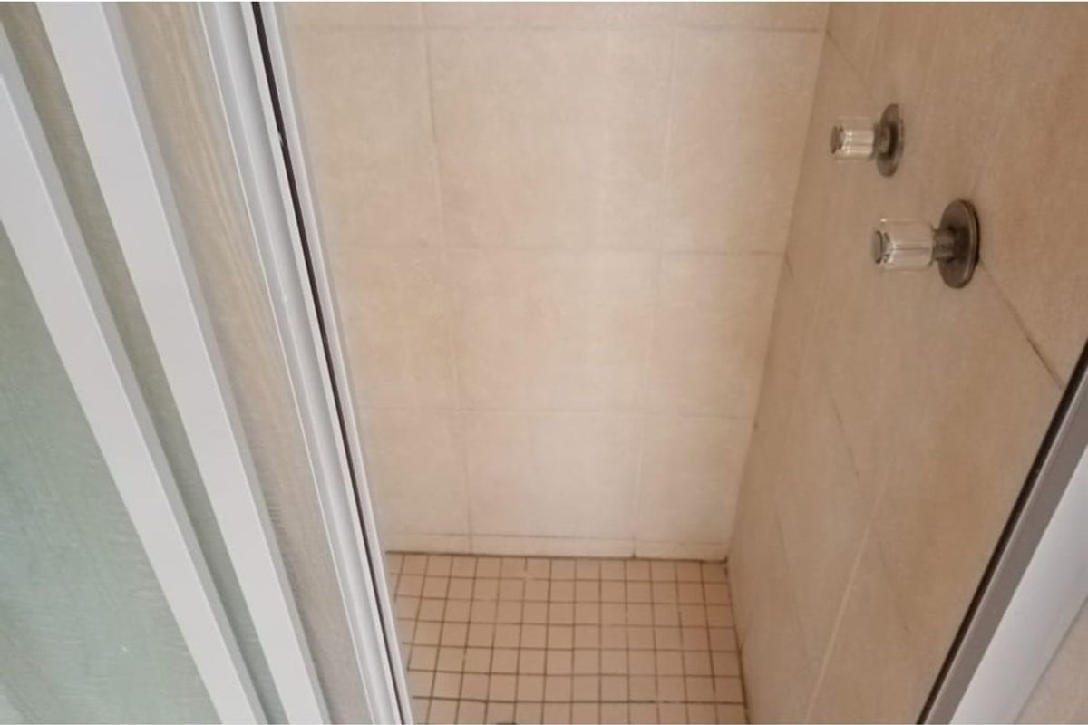 A compact shower stall featuring tiled walls and flooring with standard mixer tap fixtures, requiring some maintenance or cosmetic updates.