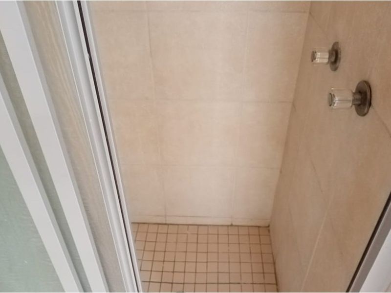 A compact shower stall featuring tiled walls and flooring with standard mixer tap fixtures, requiring some maintenance or cosmetic updates.