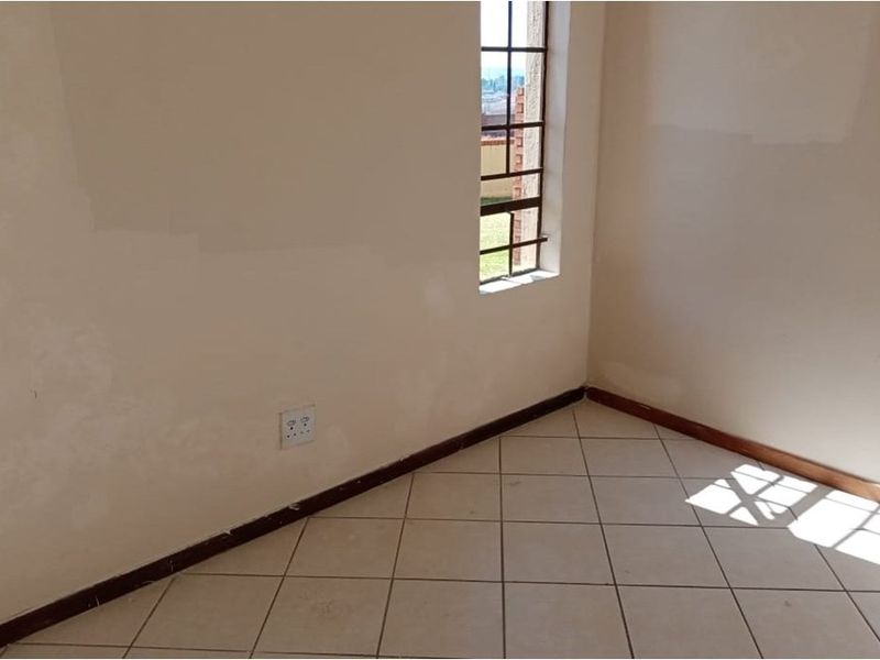 An empty bedroom featuring tiled flooring, security bars on the window, and neutral wall finishes.