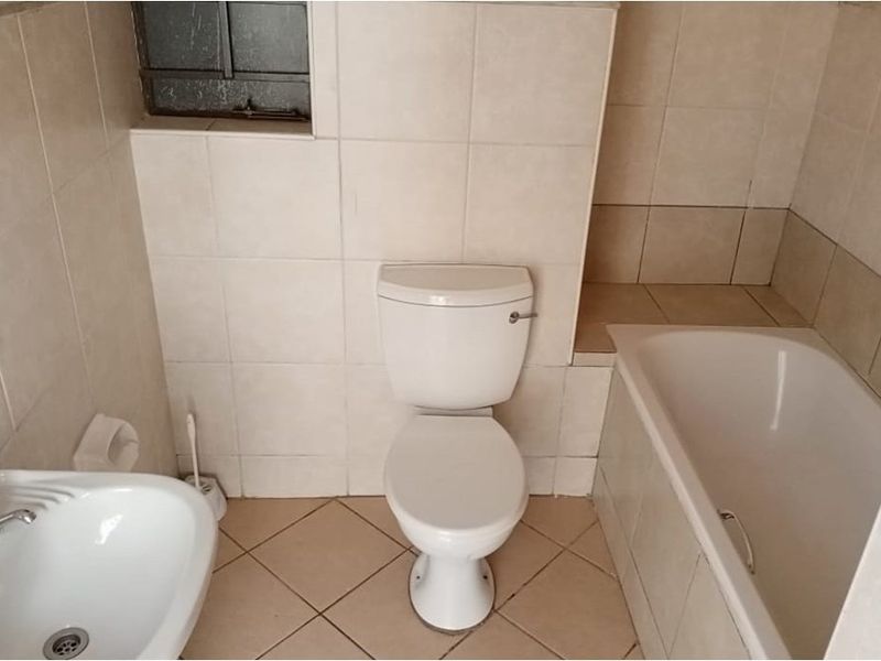 A compact bathroom featuring a standard bathtub, pedestal basin, and toilet with neutral ceramic wall and floor tiling.