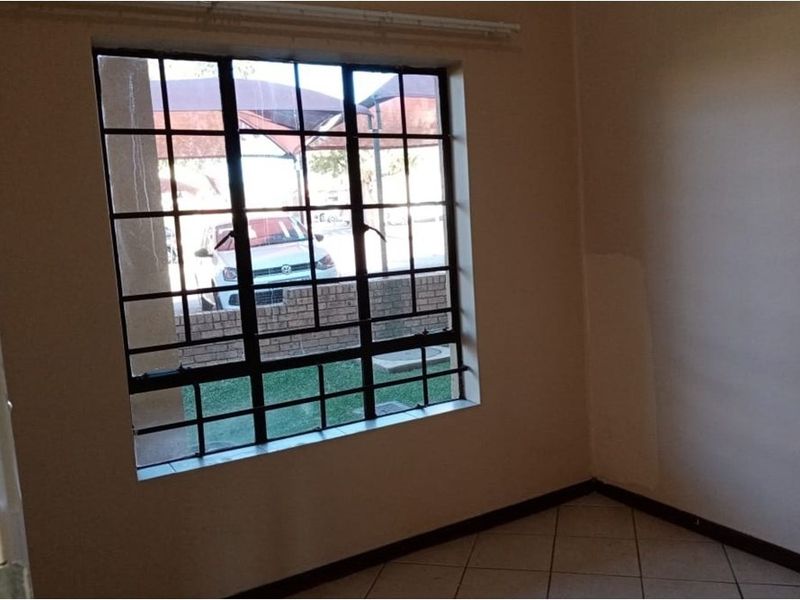 An empty bedroom featuring tiled flooring, a window with security burglar bars, and a curtain rail, requiring minor cosmetic updates to the walls.