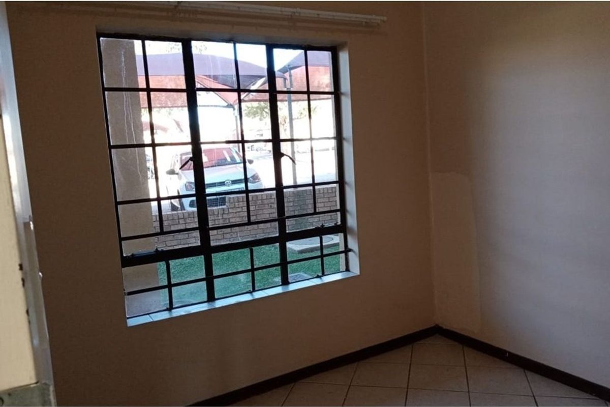 An empty bedroom featuring tiled flooring, a window with security burglar bars, and a curtain rail, requiring minor cosmetic updates to the walls.