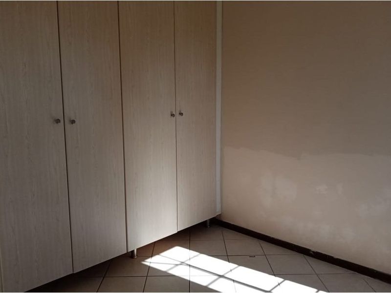 A simple bedroom featuring light-toned built-in cupboards and tiled flooring, offering a clean and functional space ready for personalization.