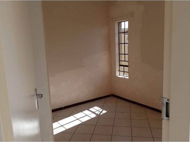 An empty bedroom featuring tiled flooring and a window with security bars, currently requiring final wall finishing and painting.