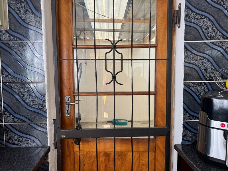 An interior entry point featuring a timber door with a security gate, flanked by decorative wall tiles and granite countertop surfaces.