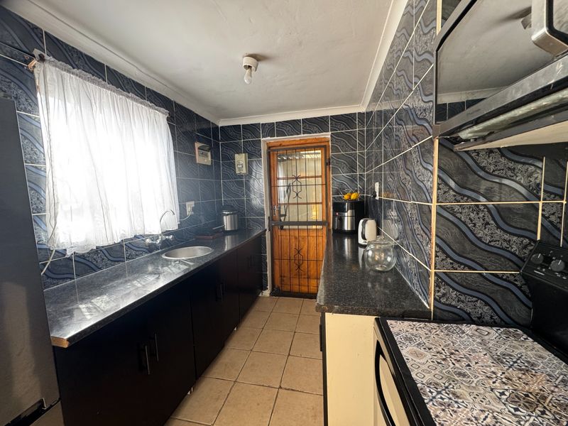 A galley-style kitchen featuring dark cabinetry, granite-look laminate countertops, tiled splashbacks, and tiled flooring with a rear security door.